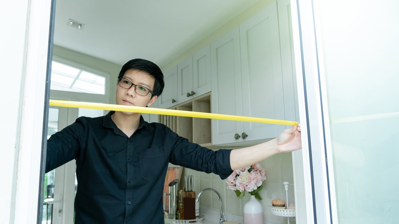 A young Asian man in a black shirt measures the doorway as he prepares to move to an apartment from a house