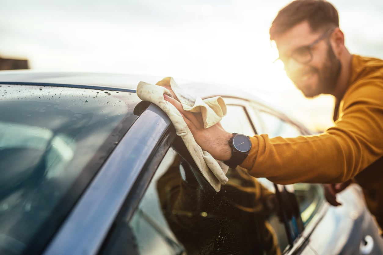A man in a yellow sweater smiles while using a cloth to get his car ready for interstate vehicle transport