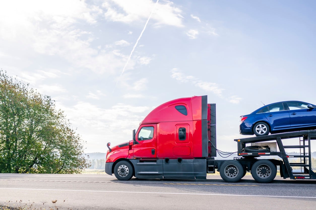 A transport trailer carries a blue sedan, showing a popular option for those who want to know how to transport your car