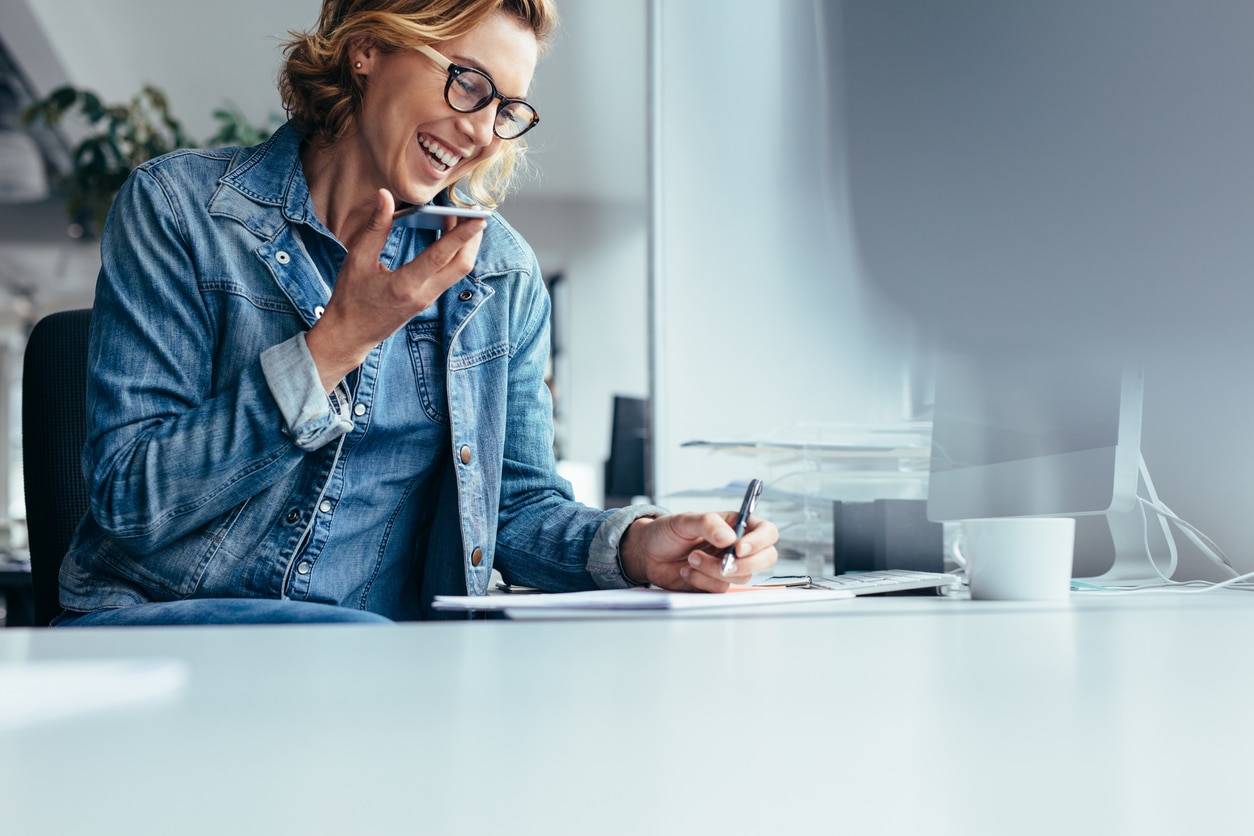 A woman in a denim jacket using speakerphone and taking notes on how to transport a vehicle to another state