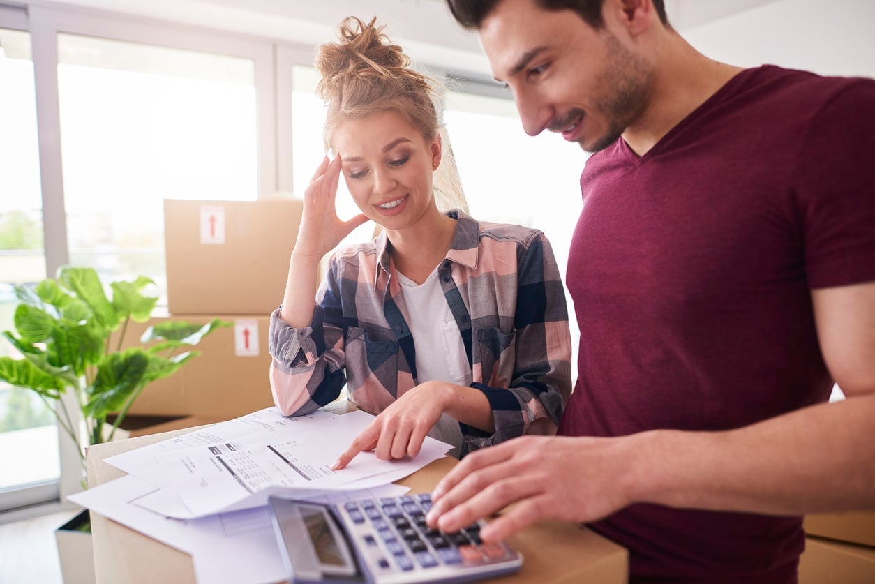 A smiling couple stands together reviewing documents on a stack of moving boxes in preparation for their DIY move