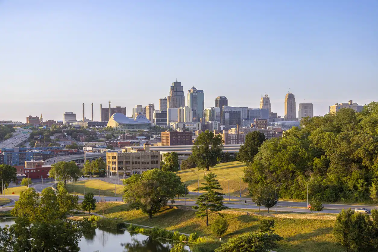 A vibrant panorama of the Kansas City skyline, featuring downtown buildings, lush green parks, and a tranquil lake