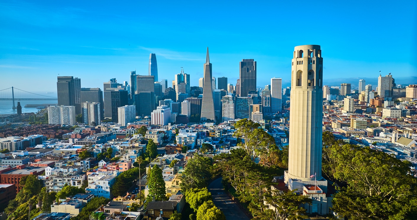 Coit Tower in San Francisco with the Transamerica Pyramid and Bay Bridge under a clear sky