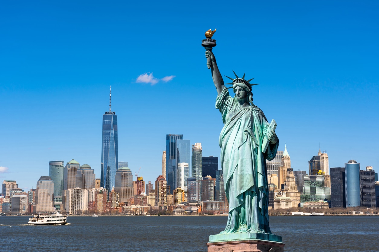 The Statue of Liberty on Liberty Island in New York Harbor, with the Manhattan skyline on a sunny day