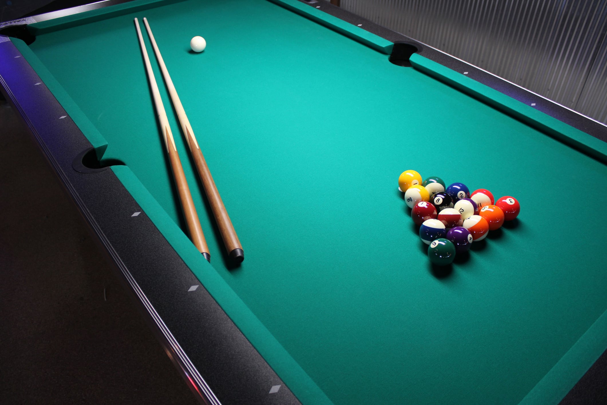 A pool table with a triangular arrangement of colorful billiard balls and two pool cues, ready