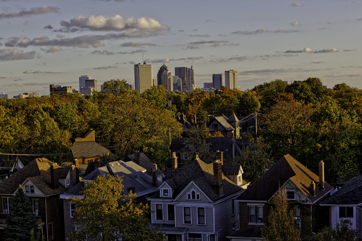 Columbus on top Columbus, Ohio skyline at sunset, viewed over a leafy residential neighborhood with historic rooftops