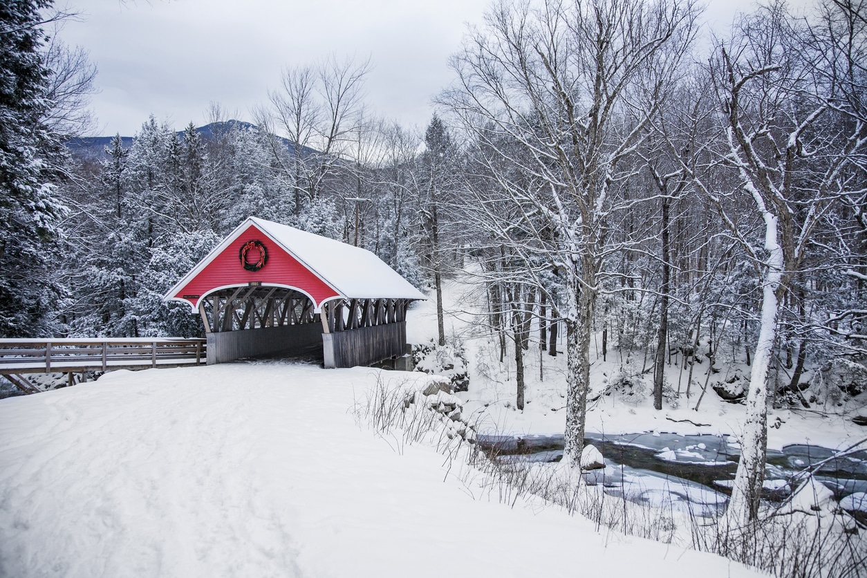 snow covered bridge Snow-covered red covered bridge over a stream in winter landscape, scenic view for those living in New Hampshire
