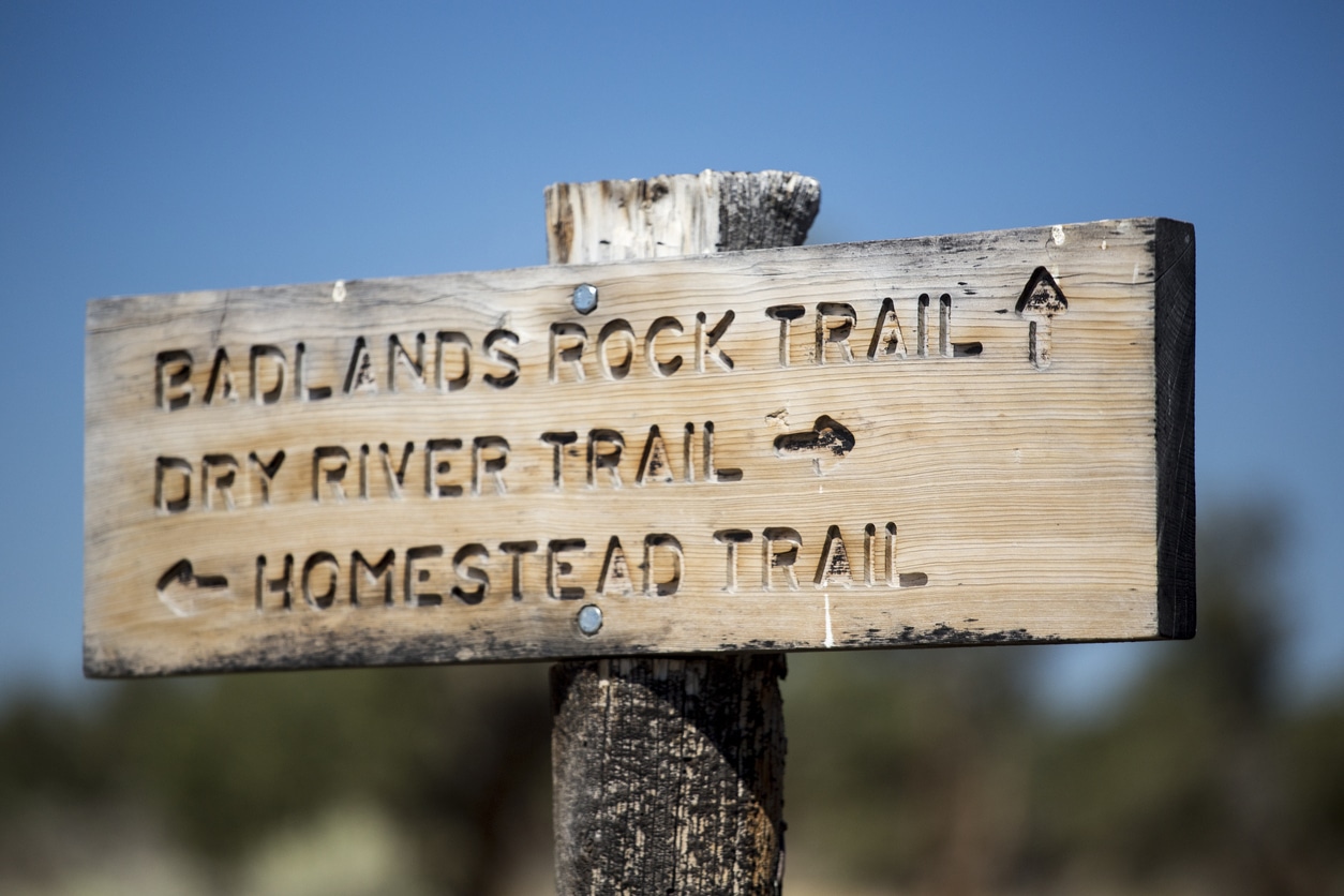 A weathered wooden signpost indicates directions for the Badlands Rock, Dry River, and Homestead trails in Oregon