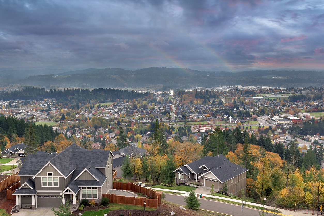An aerial view of a suburban Oregon town in a valley, surrounded by evergreen trees and autumn foliage