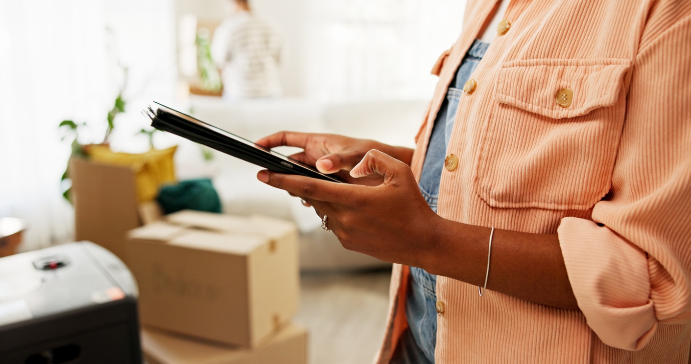 Close-up of a woman using a tablet making a moving inventory amidst moving boxes and household belongings