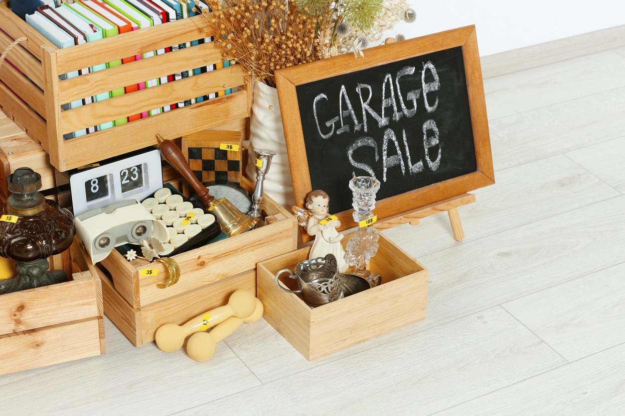 A chalkboard sign reading "GARAGE SALE" next to wooden crates filled with various secondhand items