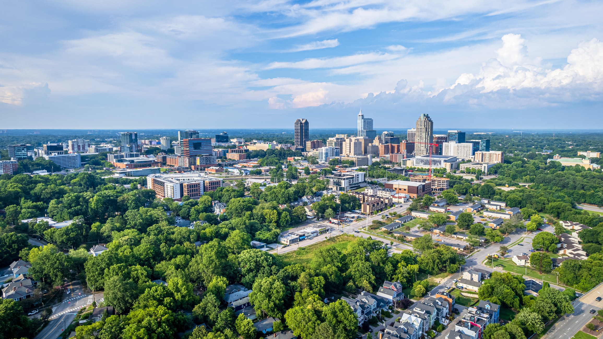 Aerial view of Raleigh, NC skyline with green spaces and homes, one of the highlights of moving to Raleigh