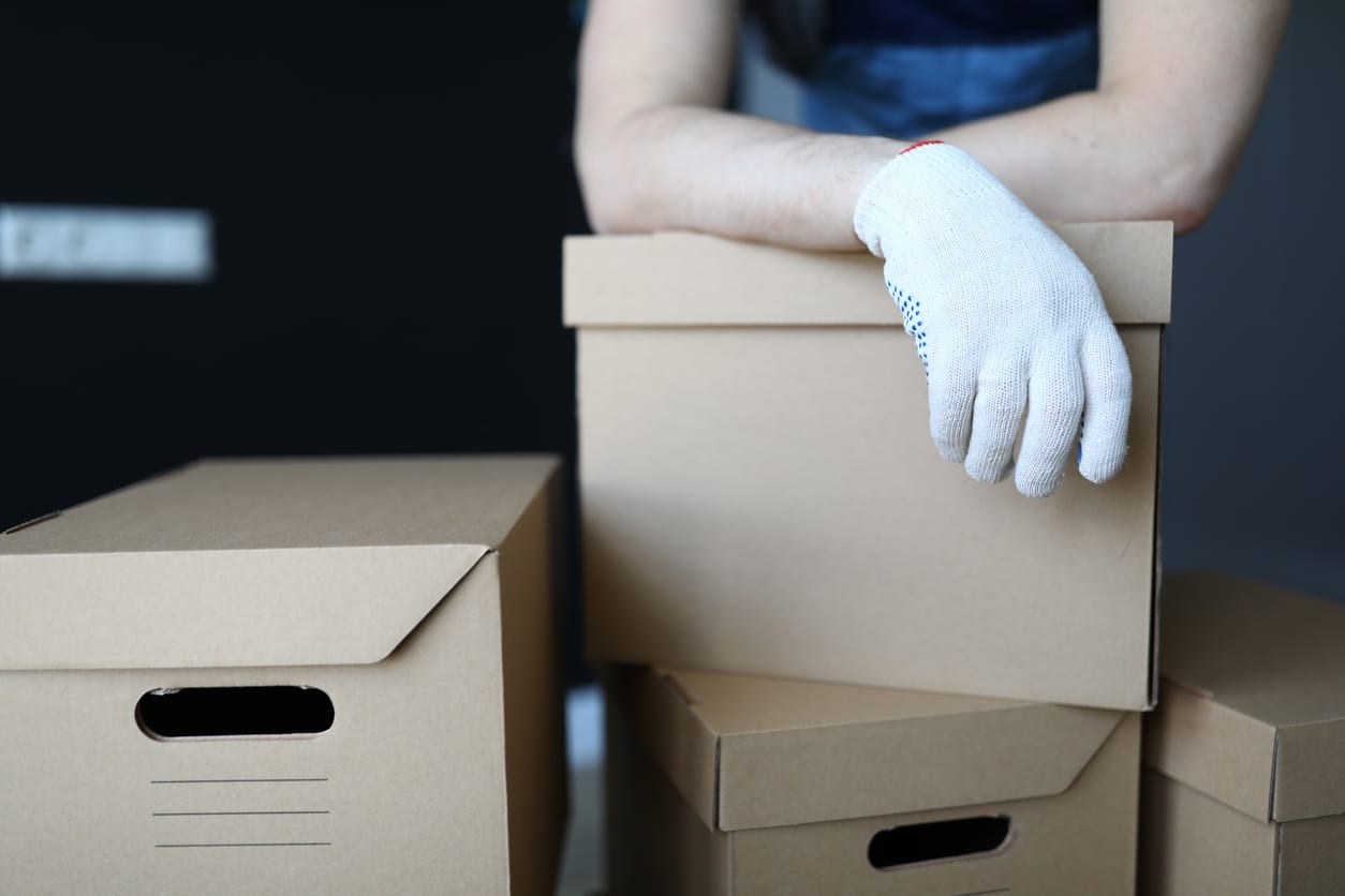 Gloved hands loader lie on cardboard boxes office Person wearing a white work glove rests hands on stacked cardboard moving boxes