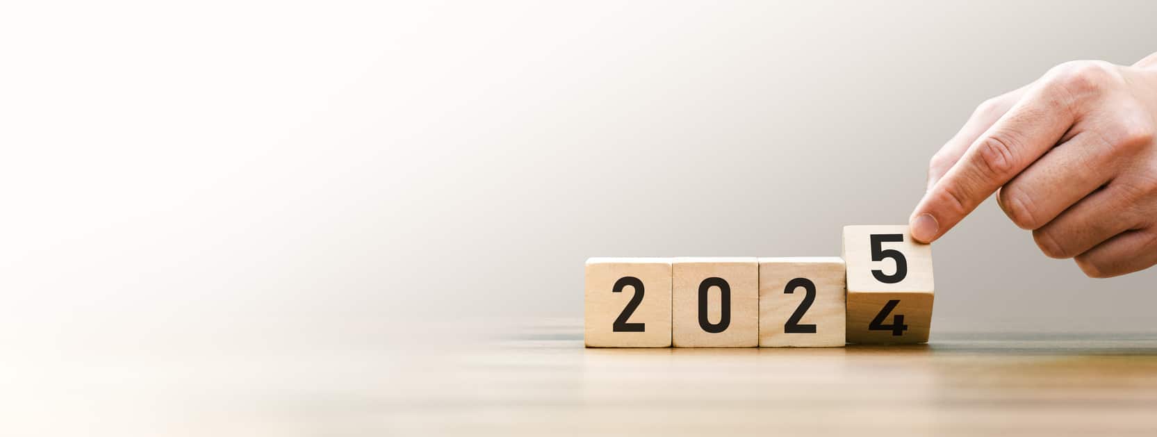 Hand placing a wooden block at the end of a series, showing the year “2025”