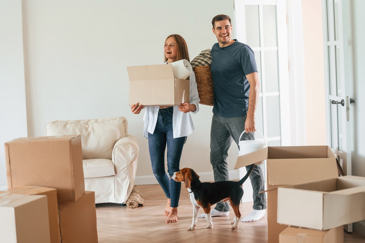 A couple in their thirties smiling as they carry boxes out of their home on moving day