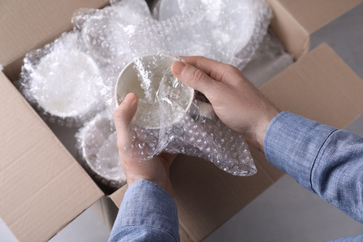 Hands wrapping a white ceramic cup in bubble wrap, preparing it for packing in a box