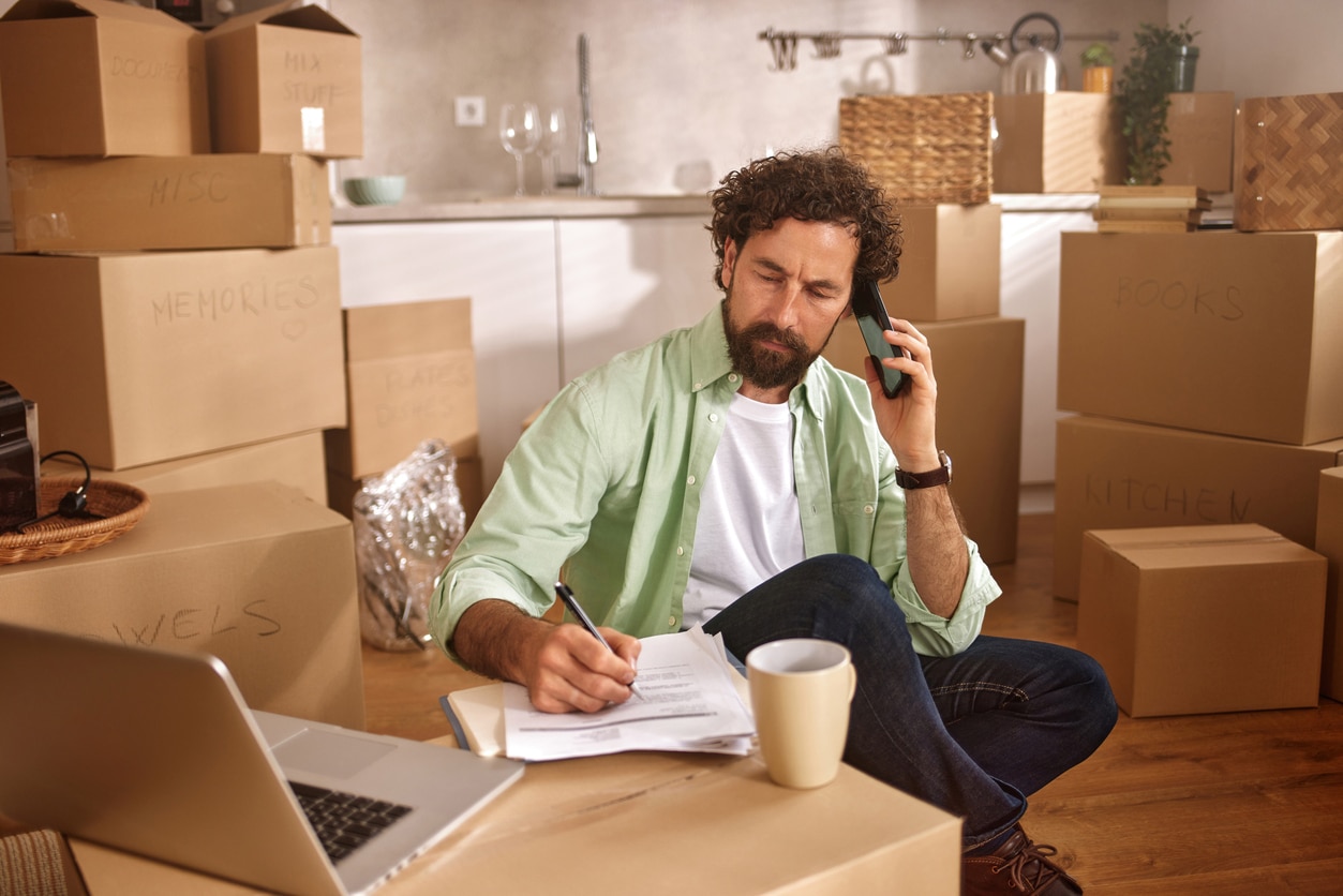A man talks on the phone and writes on documents figuring out which moving expenses are tax-deductible