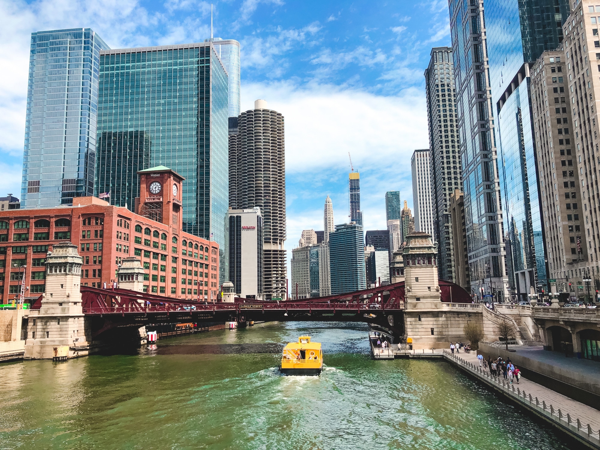 A view of downtown Chicago with skyscrapers, a red bridge, and a yellow water taxi on the river, showcasing one of the best neighborhoods in Chicago