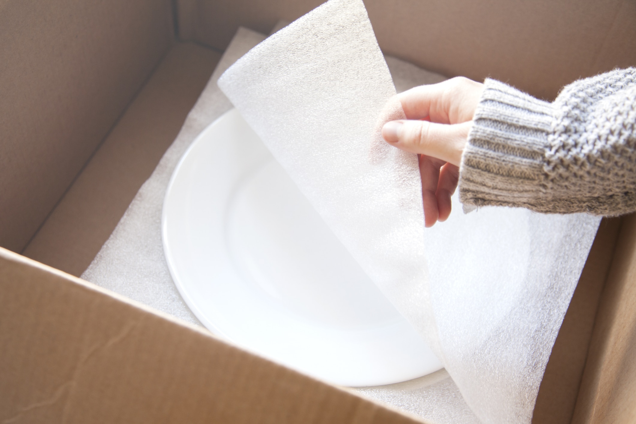 A woman demonstrating how to pack dishes for moving with white foam sheets