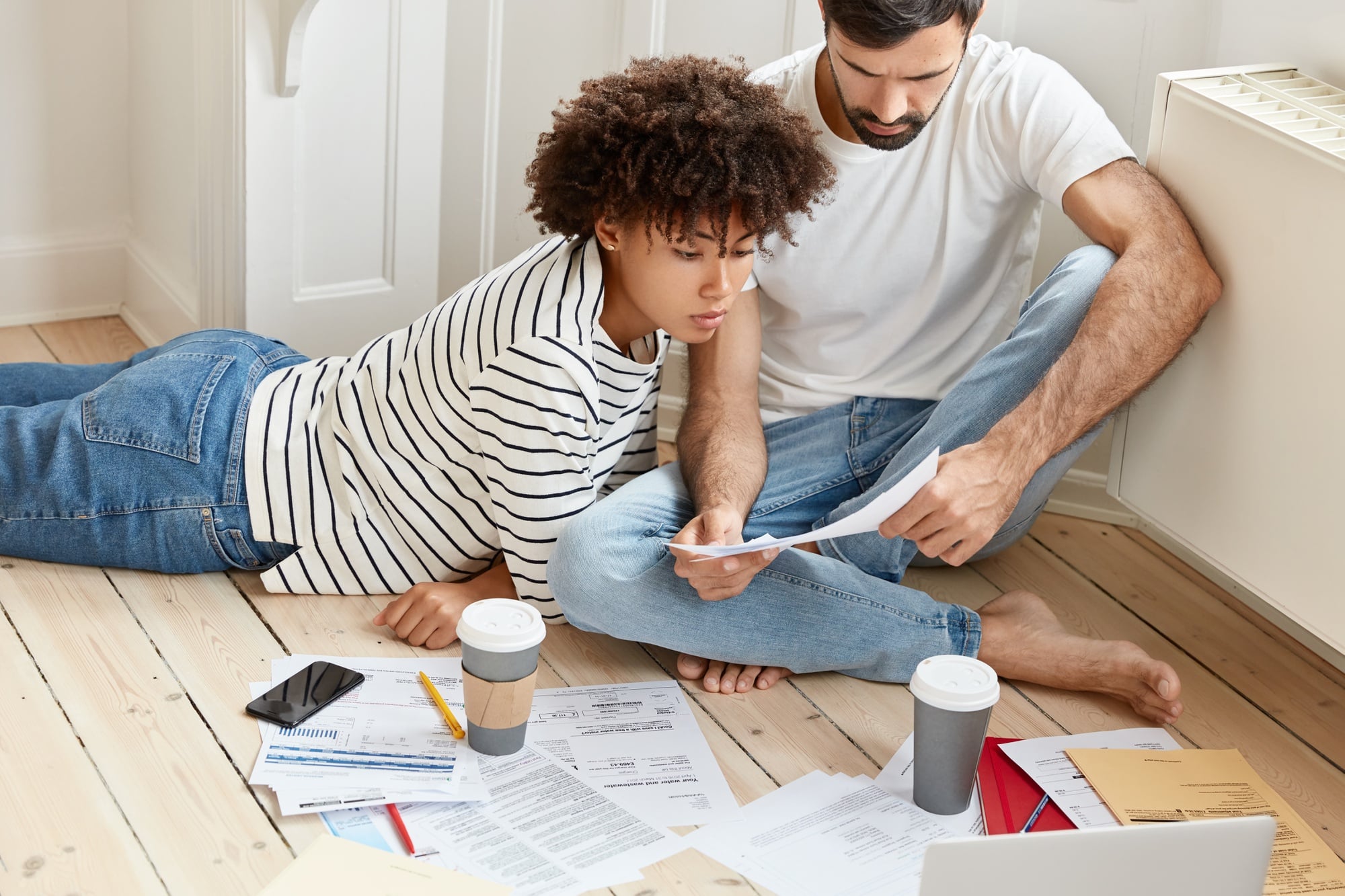 A couple sitting on the floor, working on a moving day checklist and determining their moving budget
