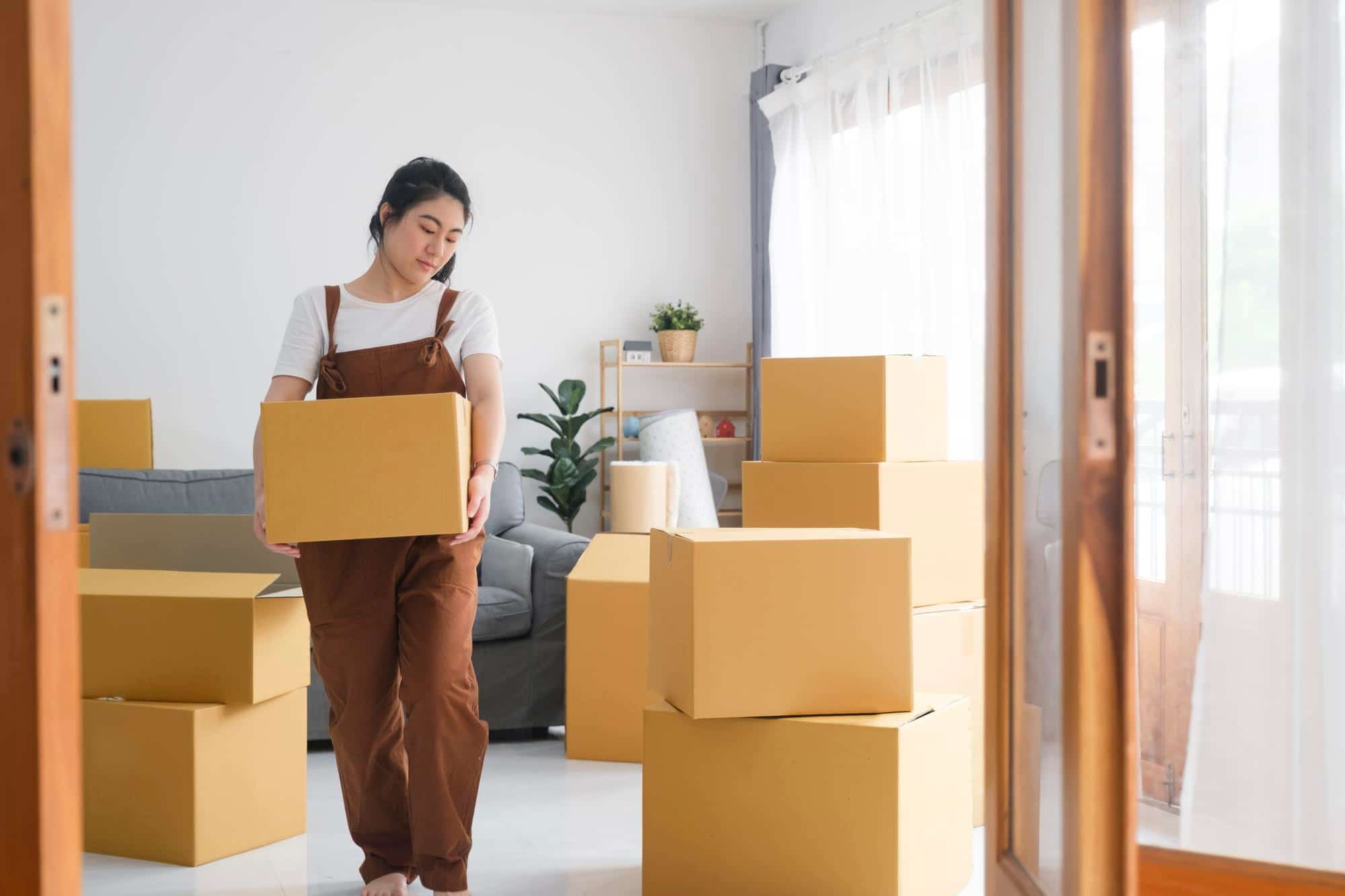 Woman carrying a box, surrounded by packed moving boxes, as she prepares to move to Texas