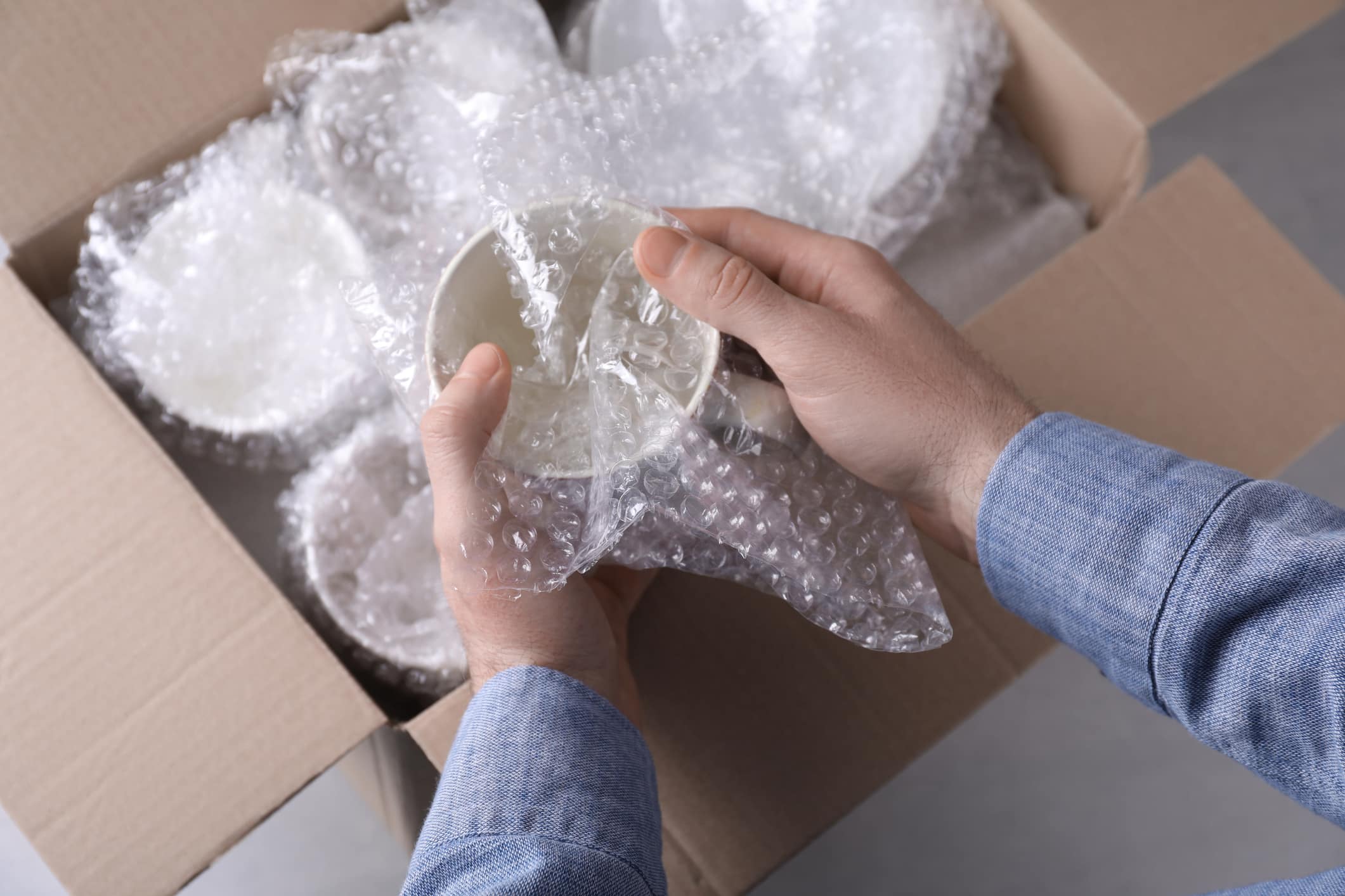 A pair of hands wrapping fragile items in bubble wrap as they pack dishes for moving