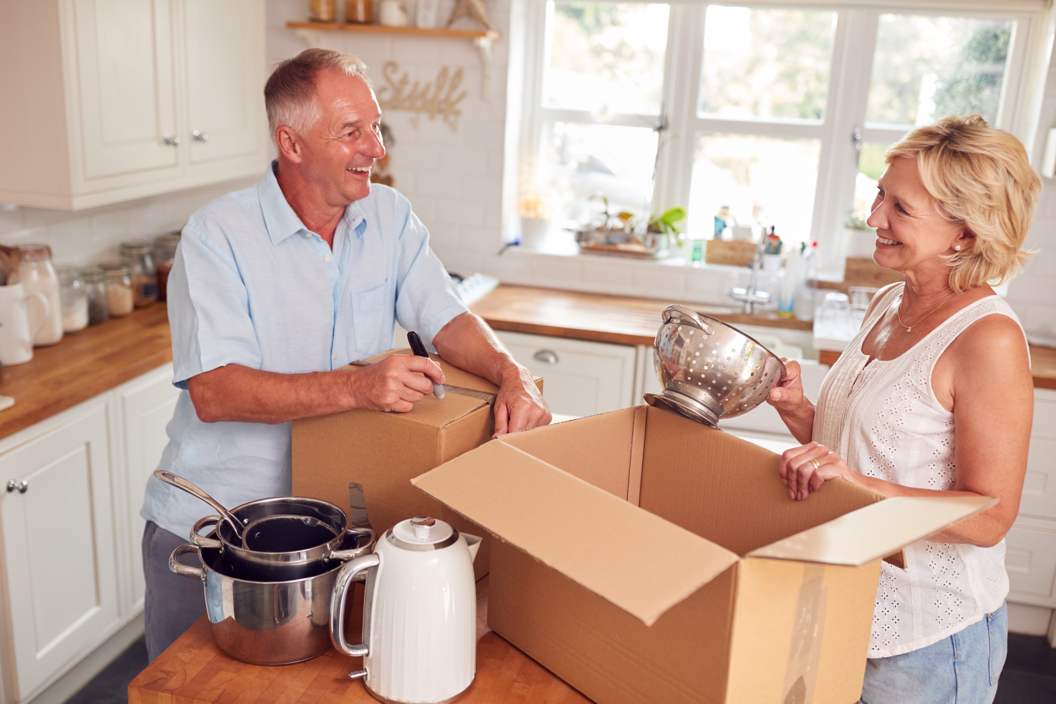 An older couple packs their kitchenware into moving boxes