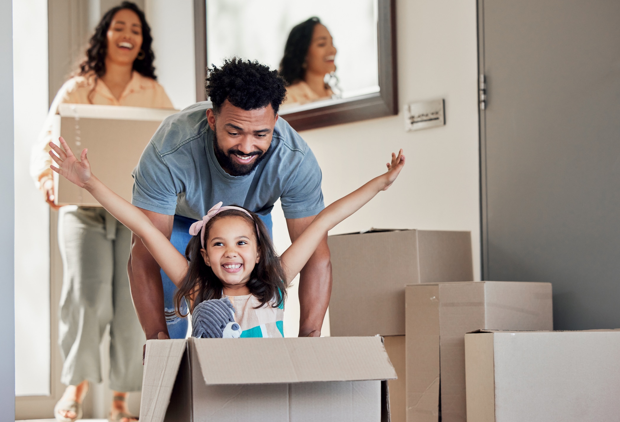 Dad playfully pushes his daughter in a moving box while mom smiles behind them, carrying a box during their move to Austin