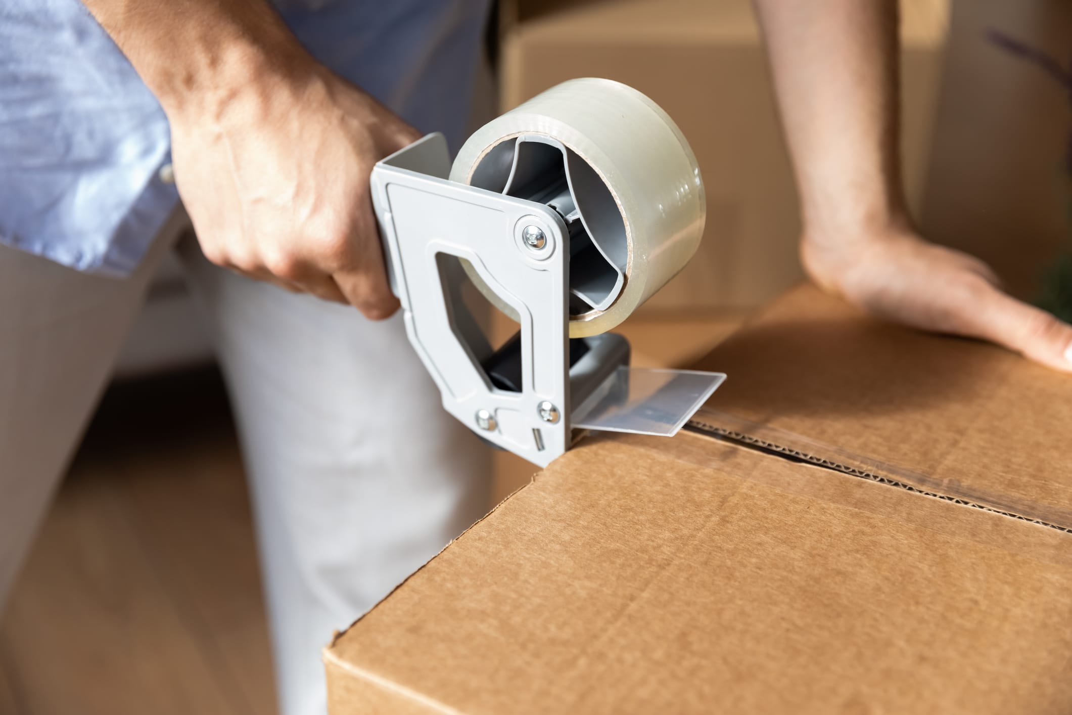 Someone using strong packing tape to securely fasten the top and bottom of boxes as they pack books for moving