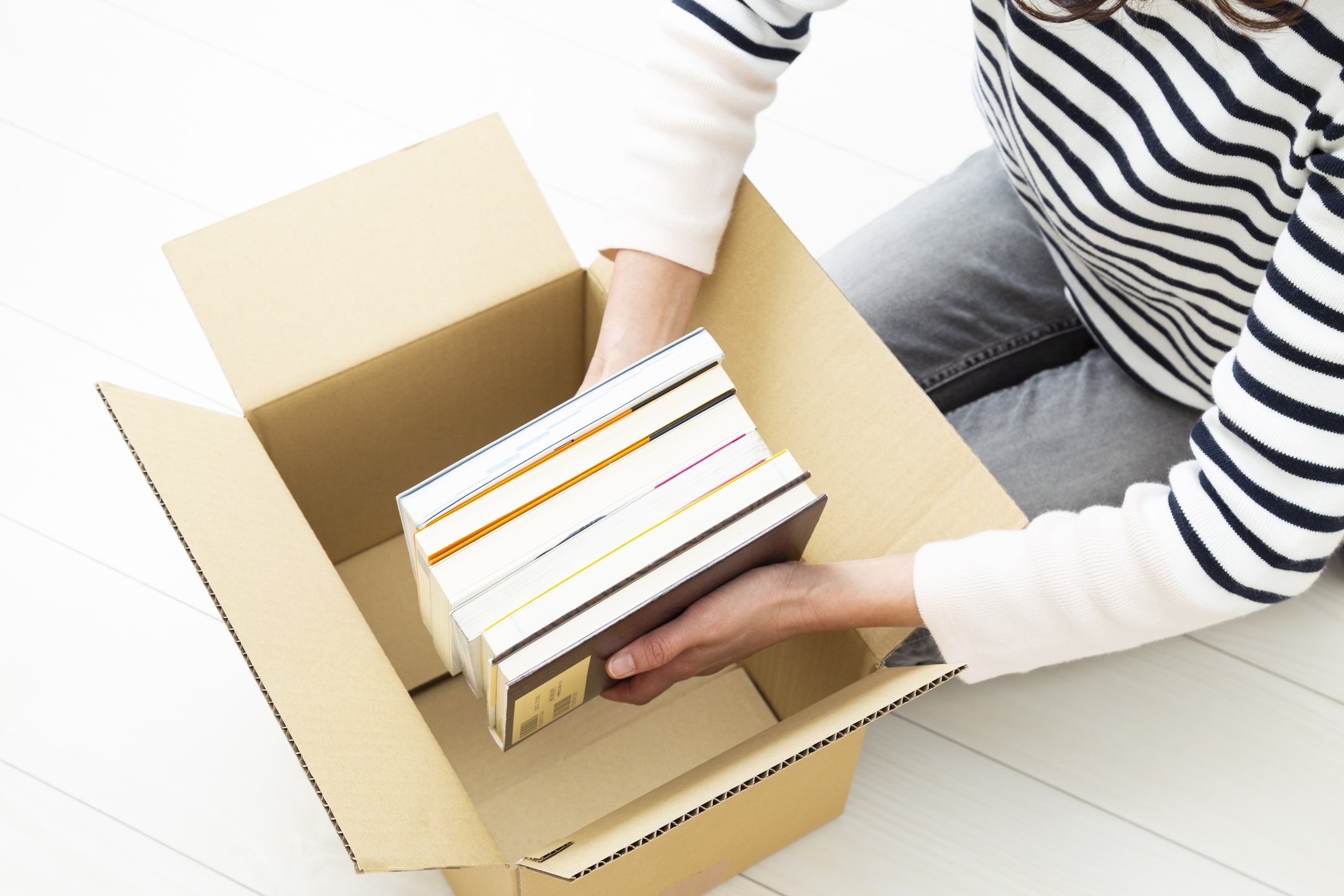 Someone carefully placing books in a moving box, showing how to pack books for moving