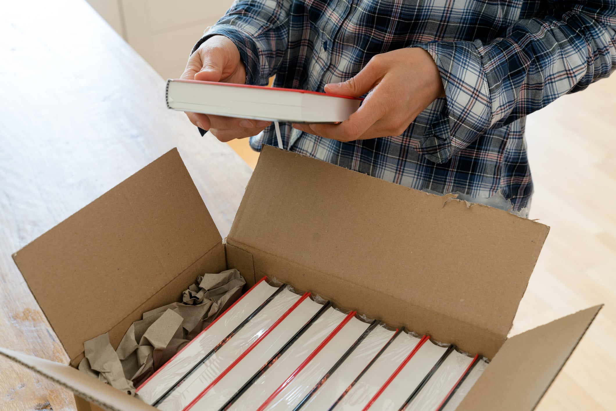 Someone packing a moving box with books vertically, spines down