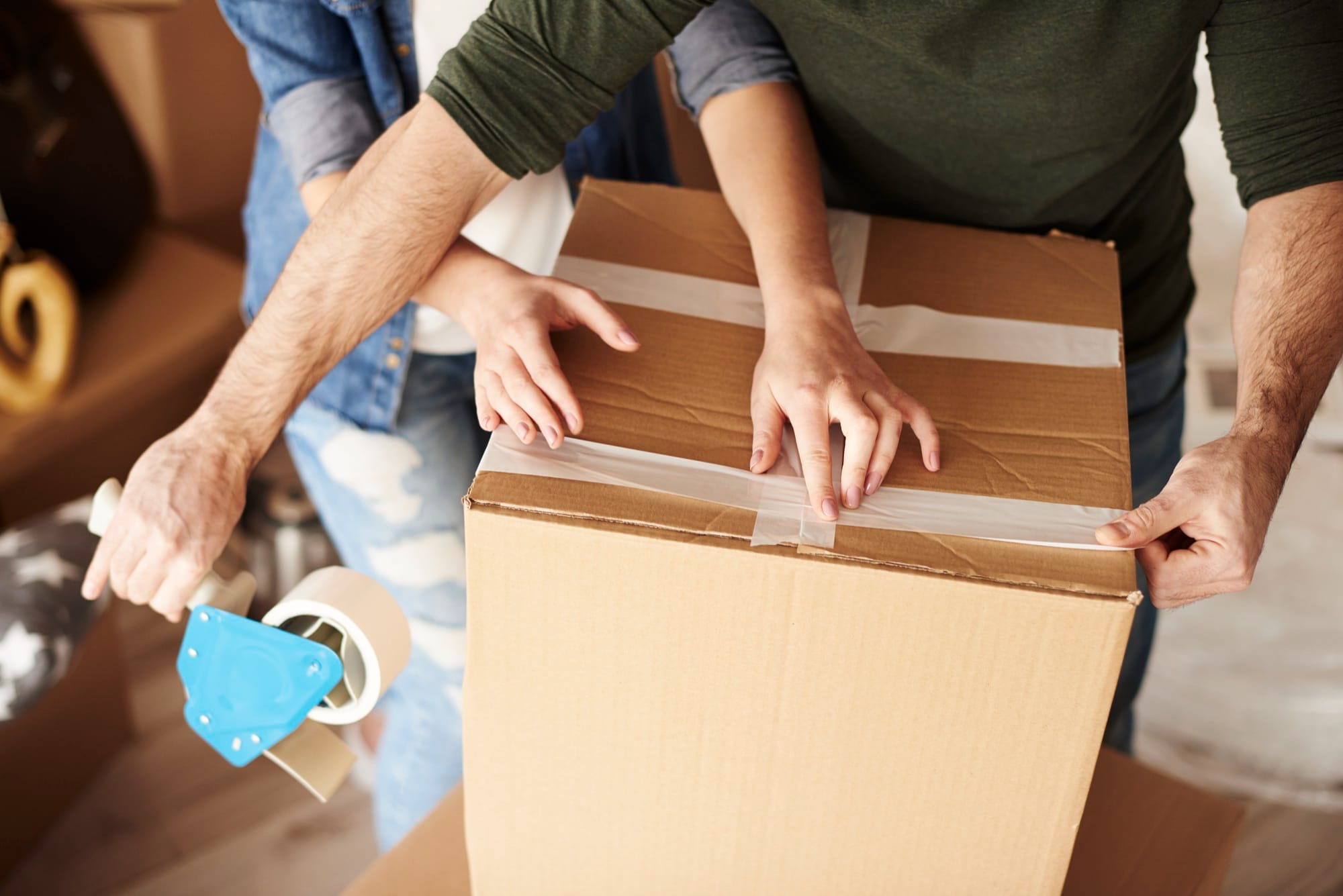 A man securing the bottom of a box with packing tape, a key step in how to pack dishes for moving