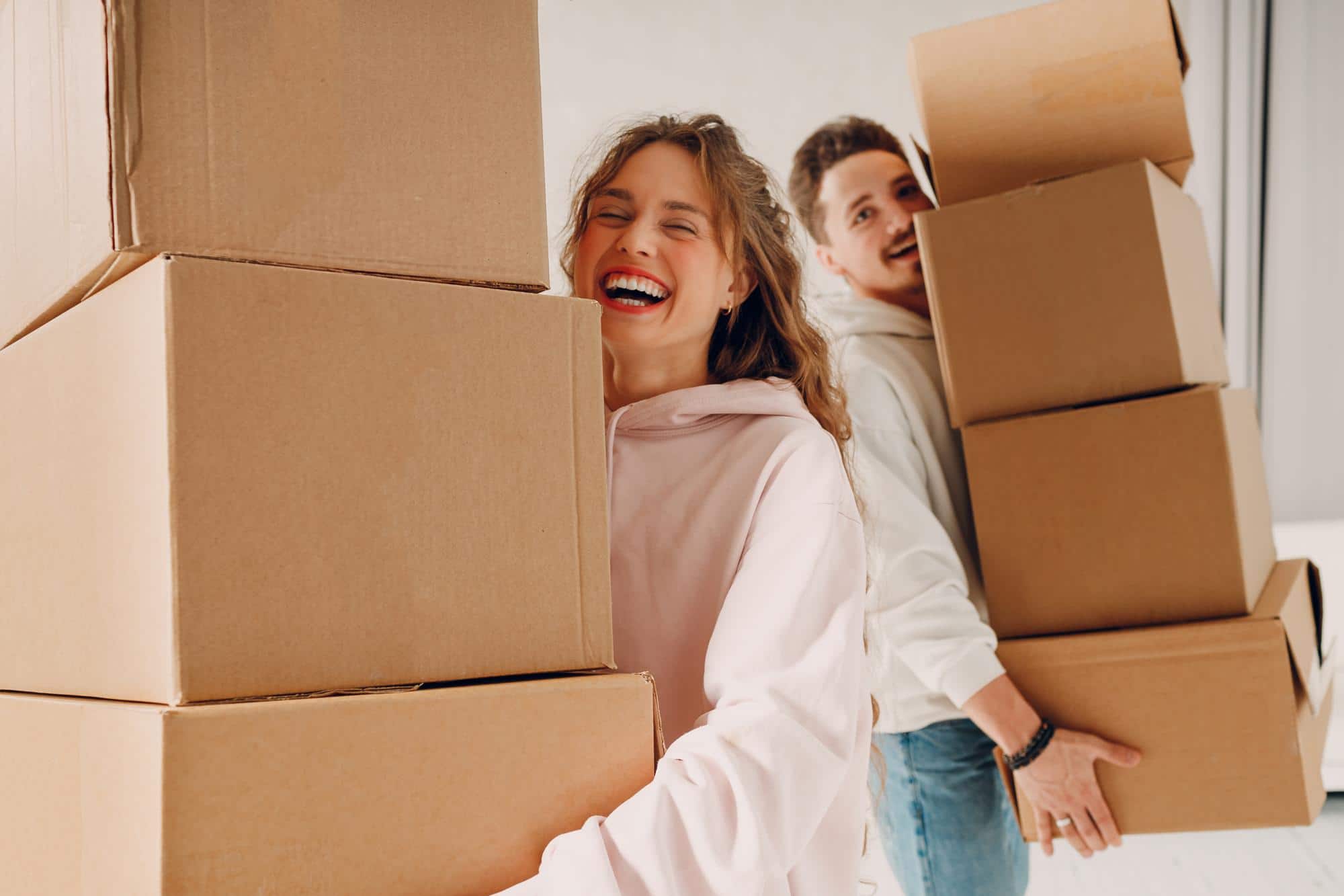 A happy couple carries stacks of moving boxes, excitedly preparing for their journey of moving to Seattle