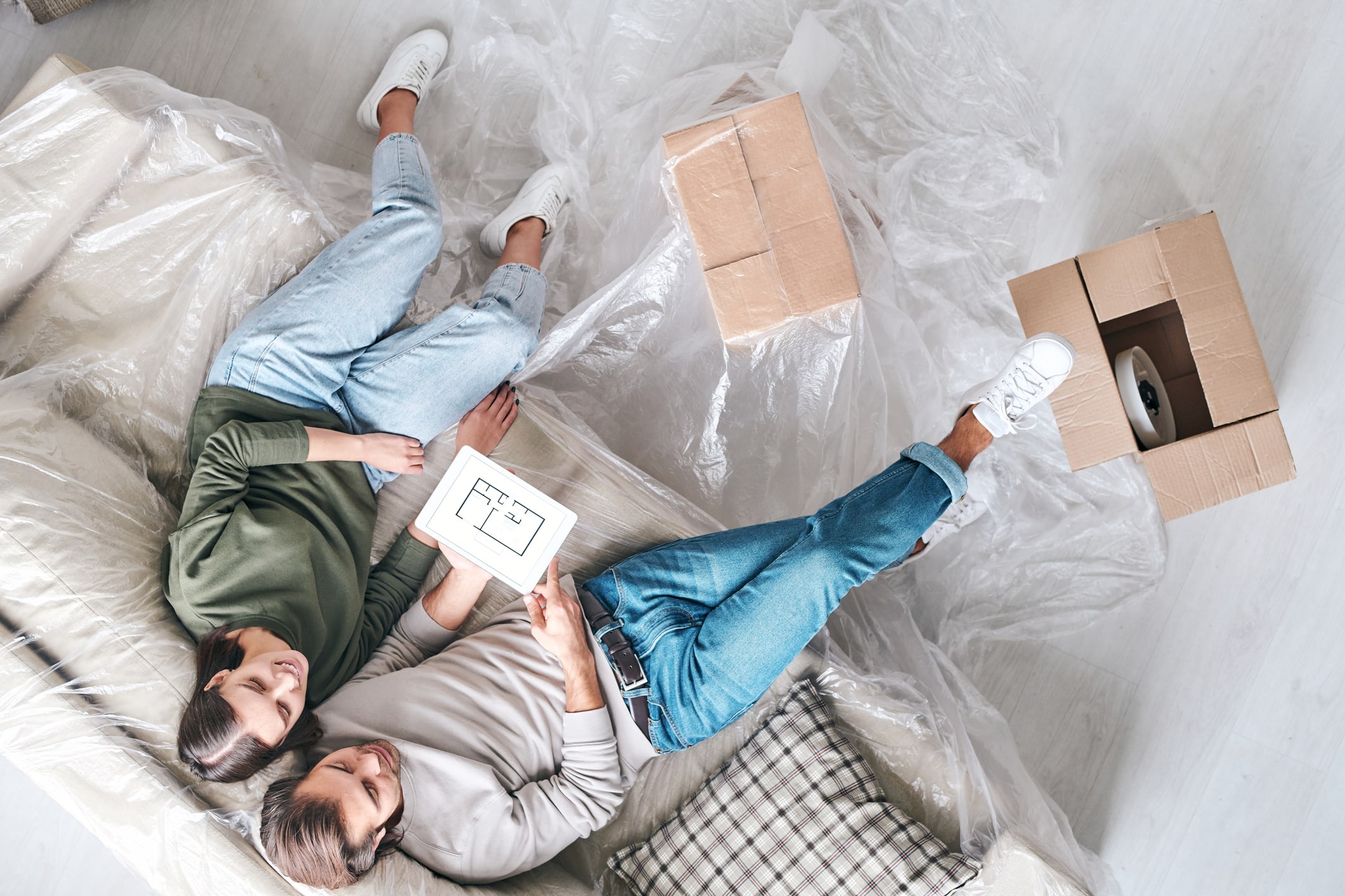 Couple relaxing in comfortable clothes on their plastic-covered couch with moving boxes around them