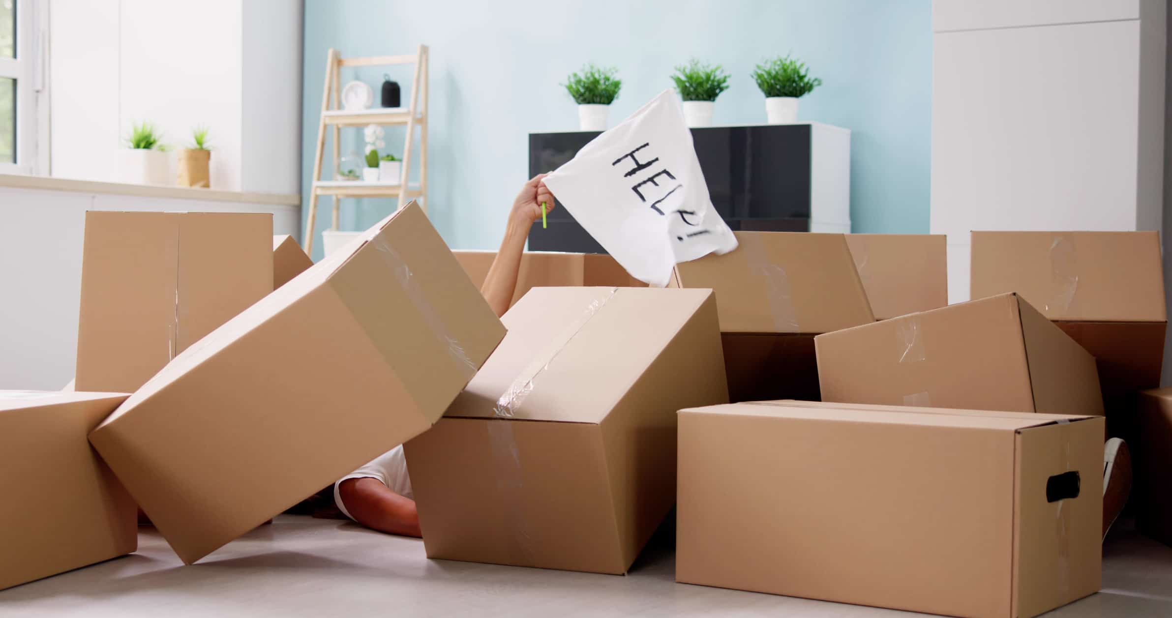 A person buried under a pile of moving boxes, waving a “help” flag