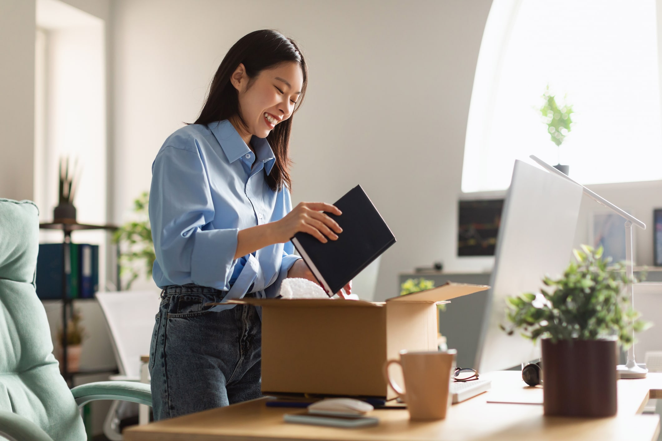 An Asian woman happily packing up her office as part of relocating for a job