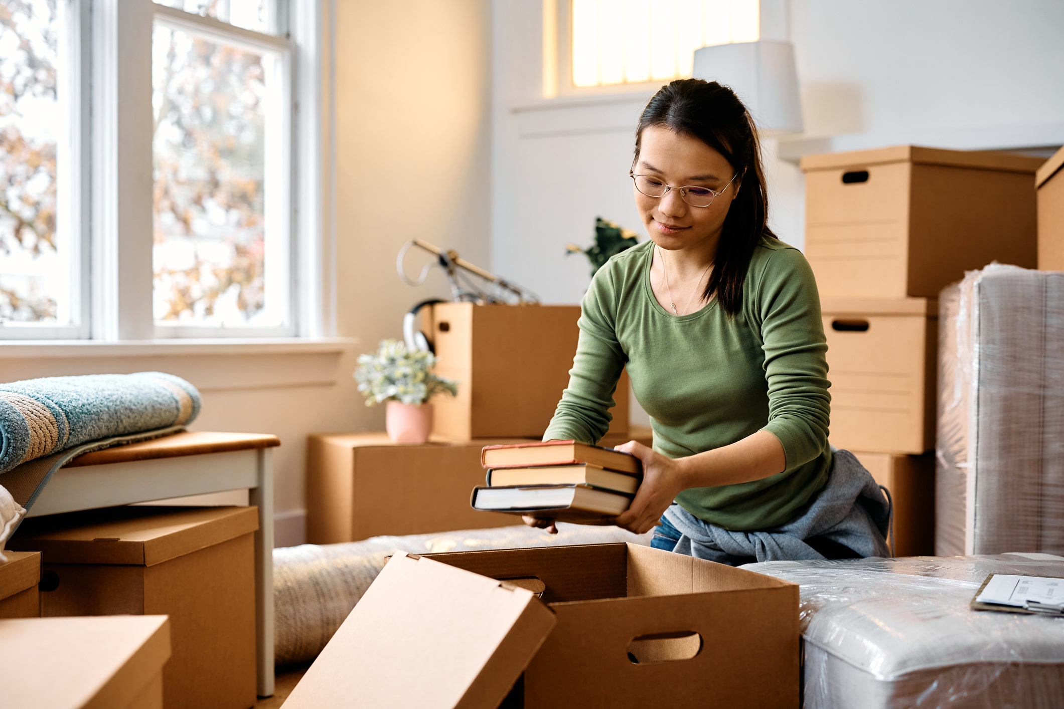 A woman happily packs her books into a moving box