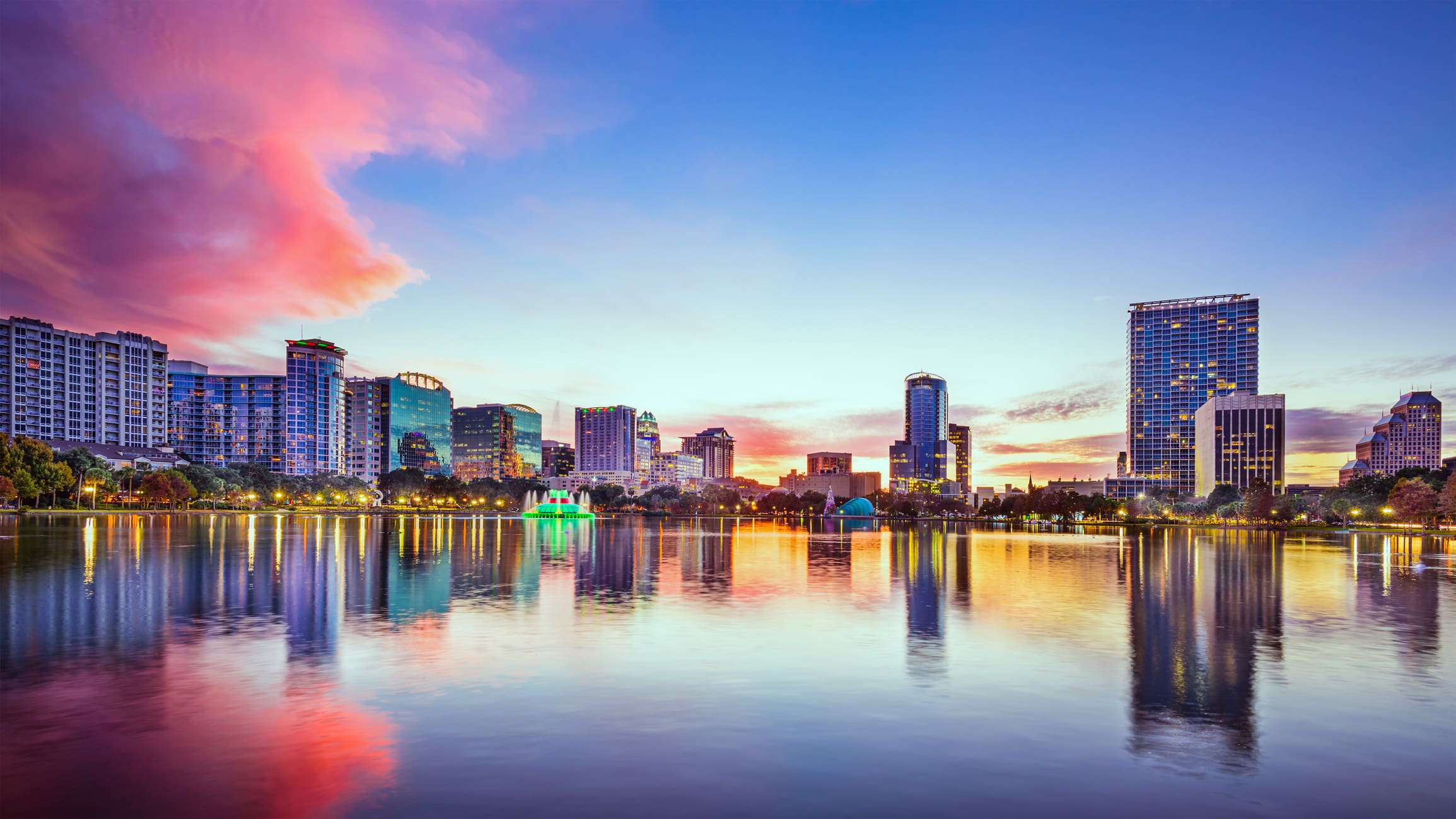 Beautifully lit up Orlando cityscape at sunset with a pink, cottony cloud in the sky