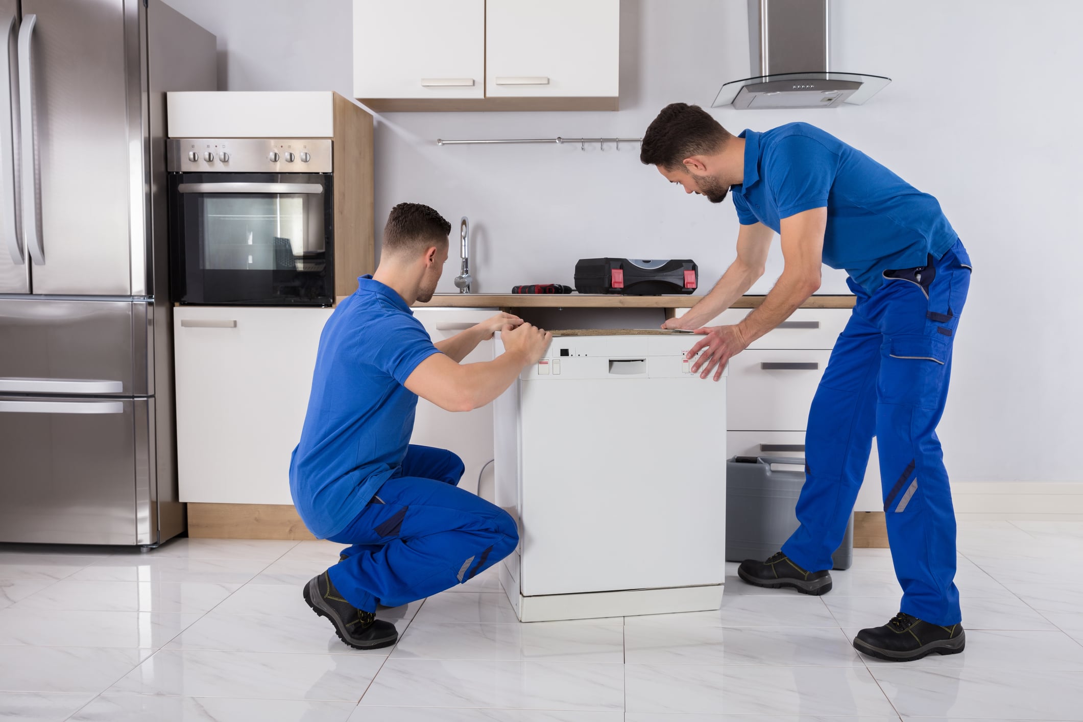 Professional movers installing a dishwasher after a long-distance move, which may incur additional moving costs