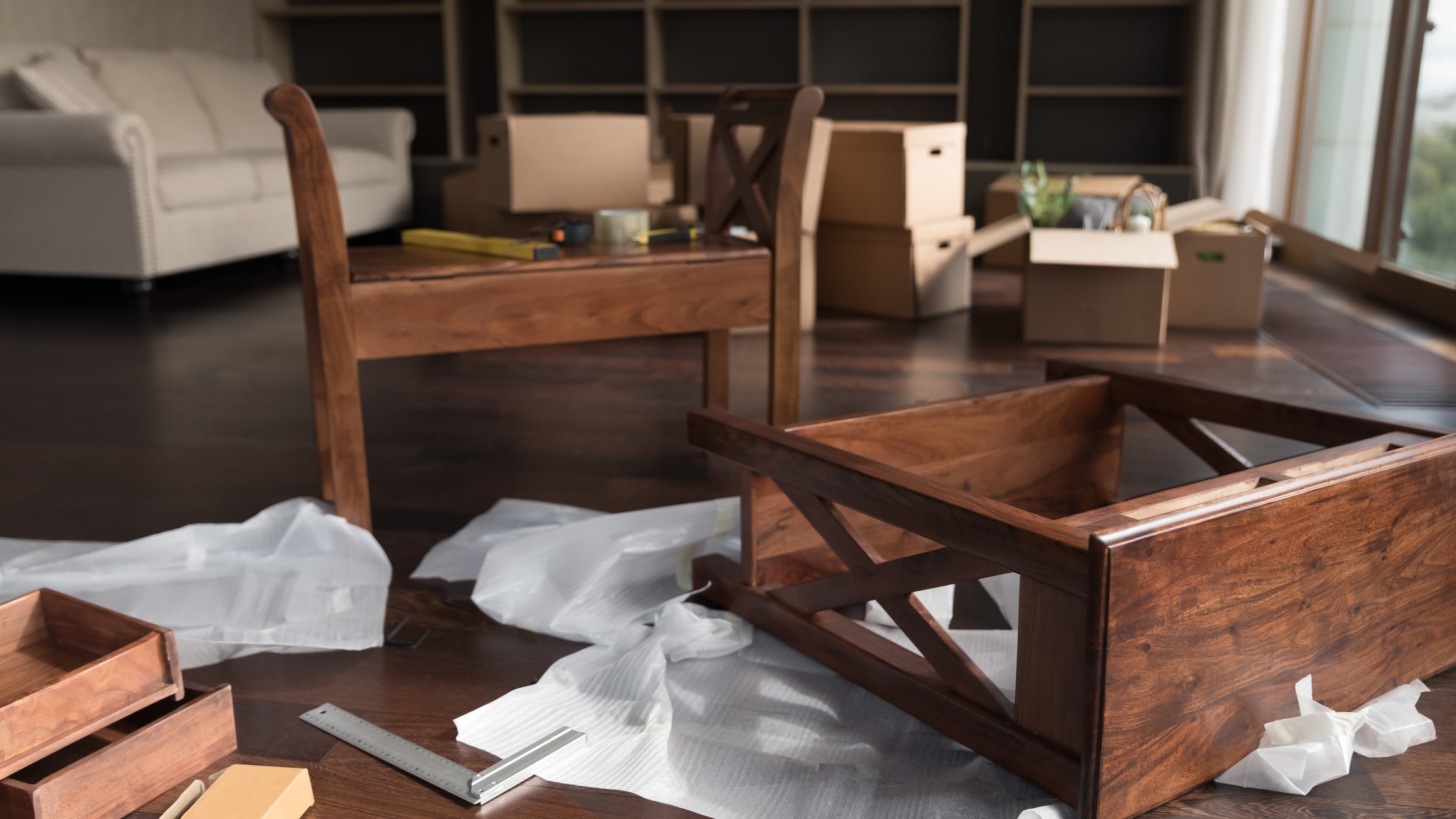 Pieces of wooden furniture, cardboard boxes for moving A living room with moving boxes, packing paper, and heavy furniture sprawled on the floor