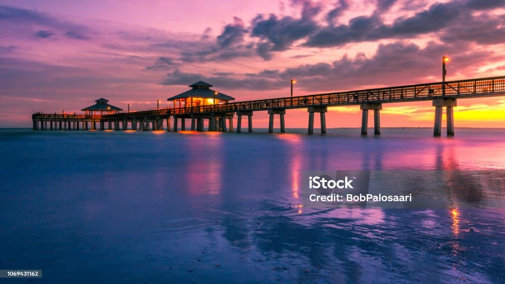 A colorful golden and purple sunset falls beneath the horizon at the Fort Myers Beach Pier in Florida, USA. Long exposure seascape background with copy space.