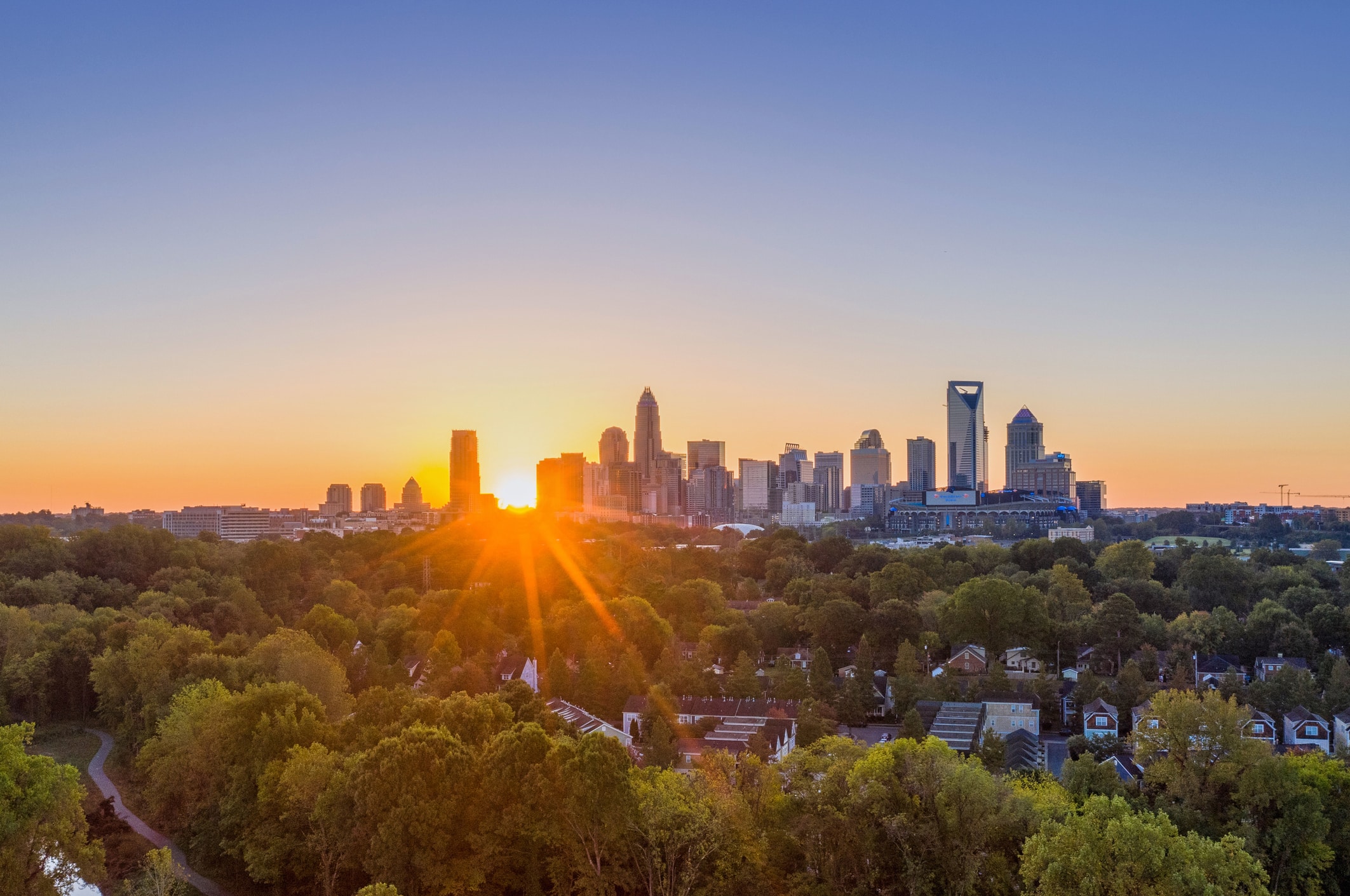 Distant view of a skyline during sunset in Charlotte, North Carolina, United States The sun setting over Charlotte, NC, with lush greenery in the foreground and downtown Charlotte in the background