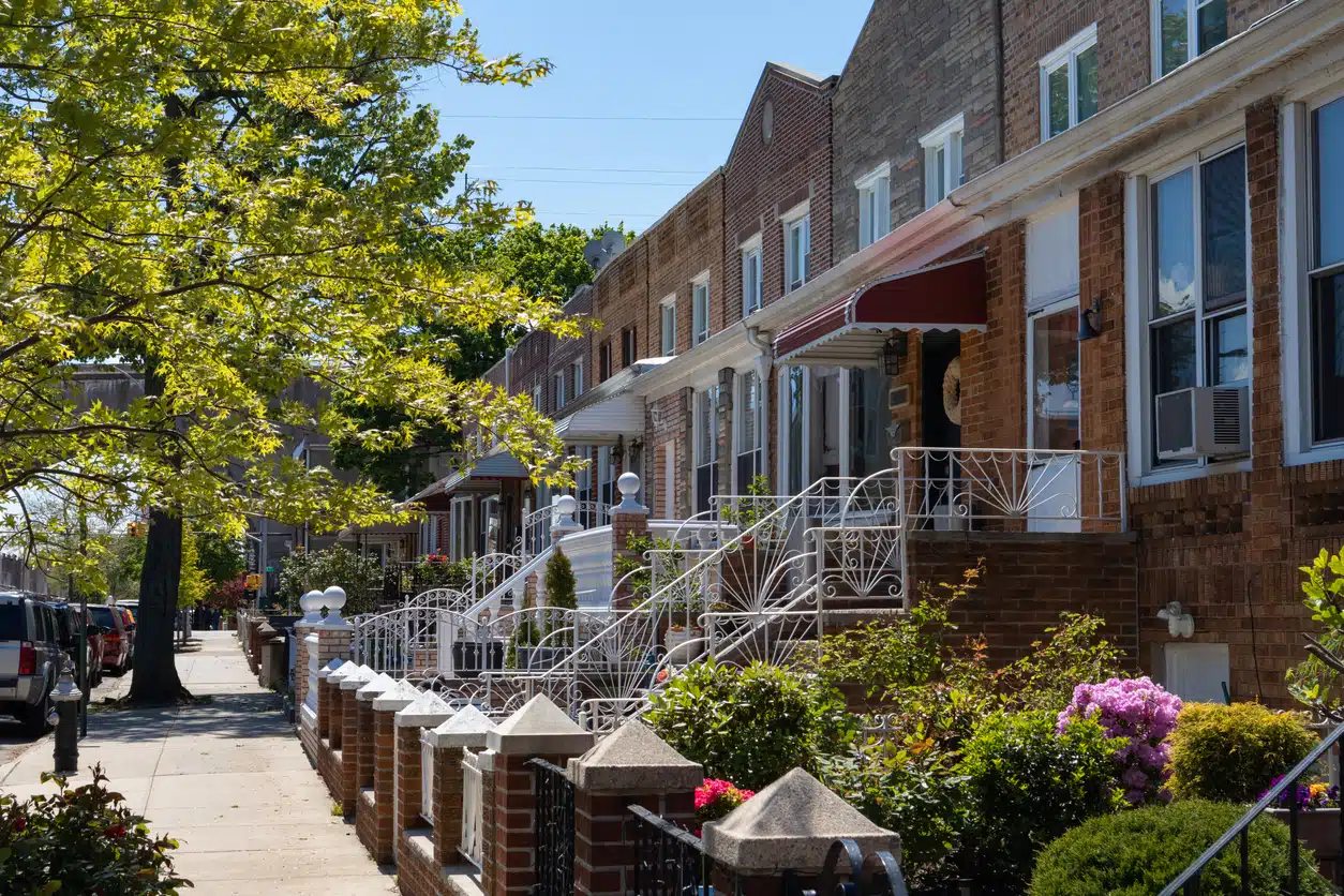 Tree-lined street in Astoria, Queens with brick row houses, blooming gardens, and classic New York charm