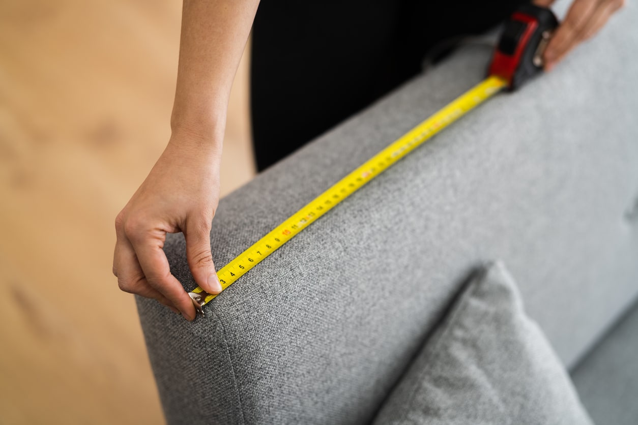 Home Improvement Sofa Size Measure Ruler A person getting ready to move a coach measuring the width of their sofa with a measuring tape