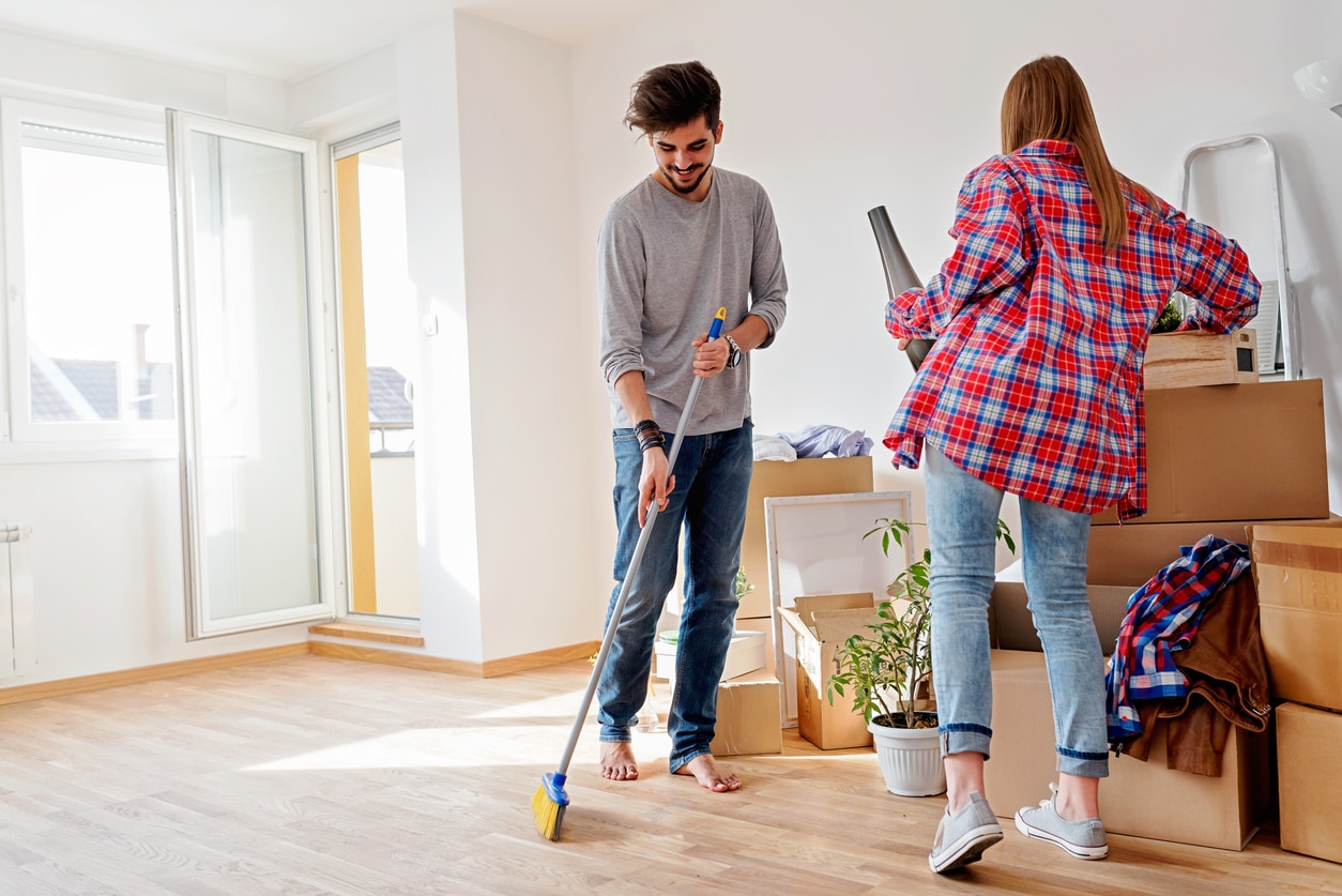 Young couple moving in new home. Unpacking box containers and cleaning. A young couple in their new home, unpacking and cleaning, with several moving boxes around them