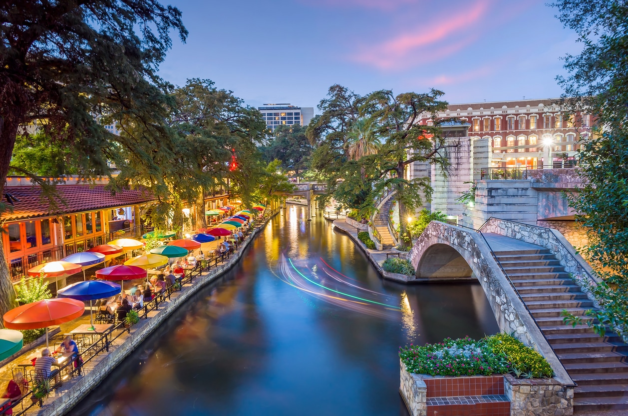 San Antonio River Walk, featuring dining under colorful umbrellas and the water reflecting the evening sky