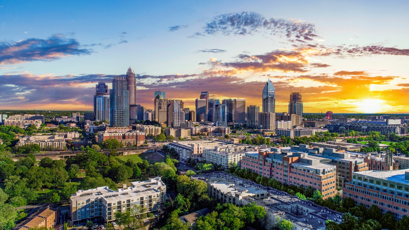 Vibrant sunset over the Charlotte, NC skyline with high-rise buildings, trees, and residential areas in view