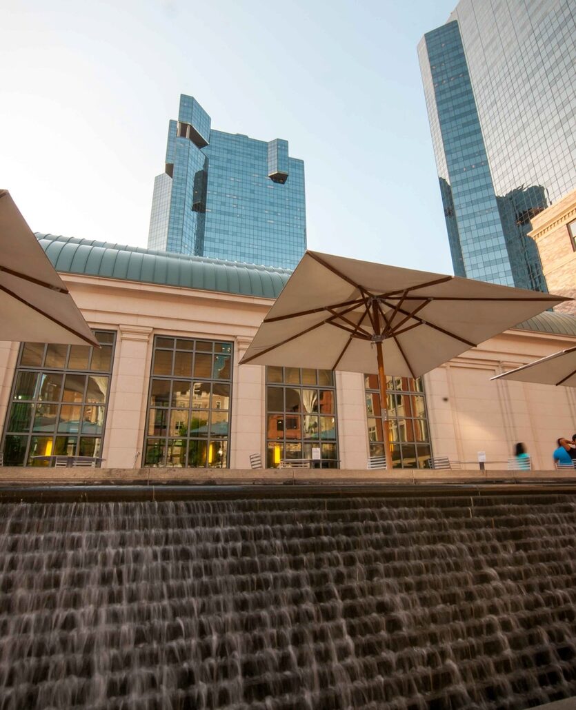 Water cascades down steps at Sundance Square in Fort Worth, with patio umbrellas and people strolling by