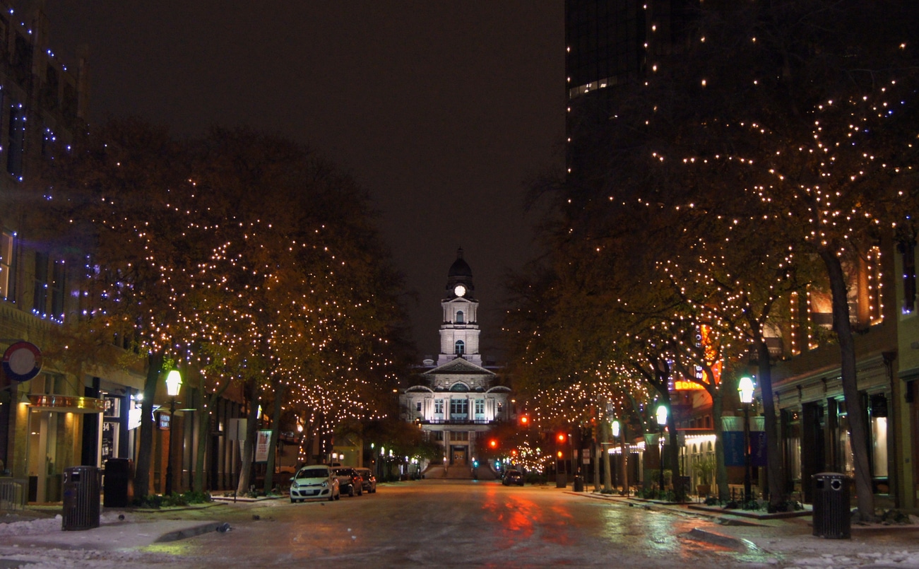 Nighttime view of Tarrant County Courthouse in Fort Worth, with icy roads and trees lit with string lights