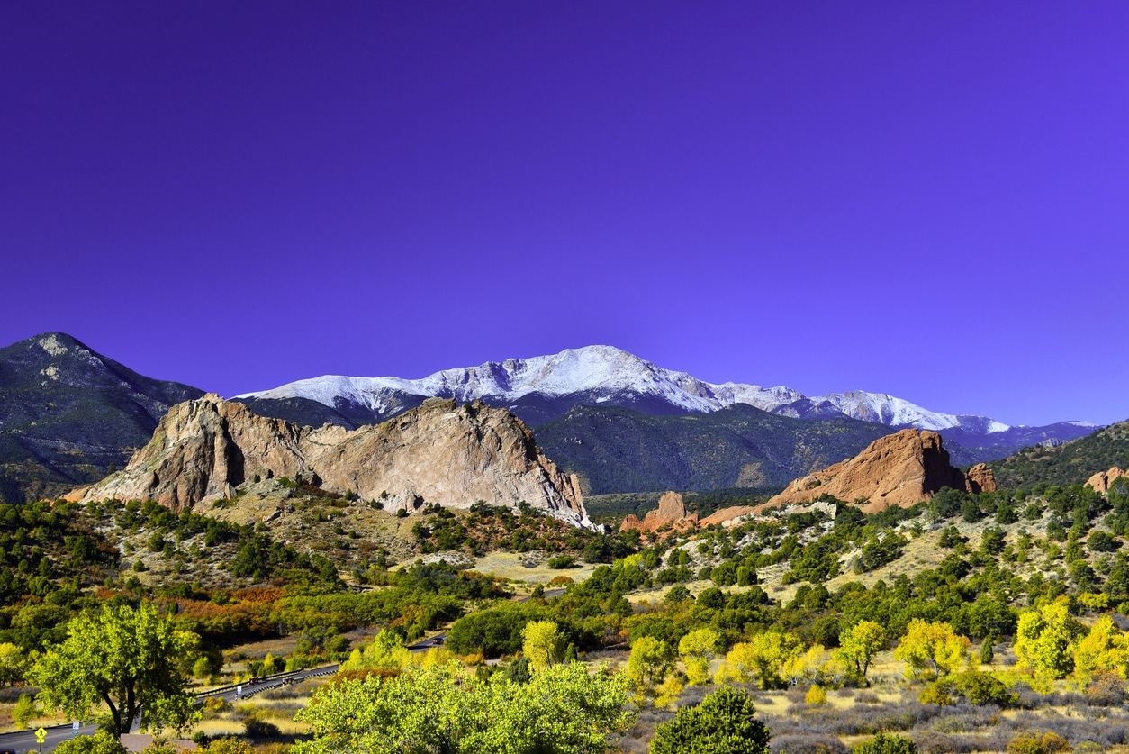 Red rock formations at Garden of the Gods with golden trees and snow-capped Pikes Peak in Colorado Springs